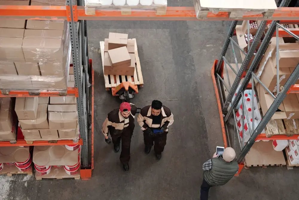 Warehouse workers moving a pallet of boxes between shelves