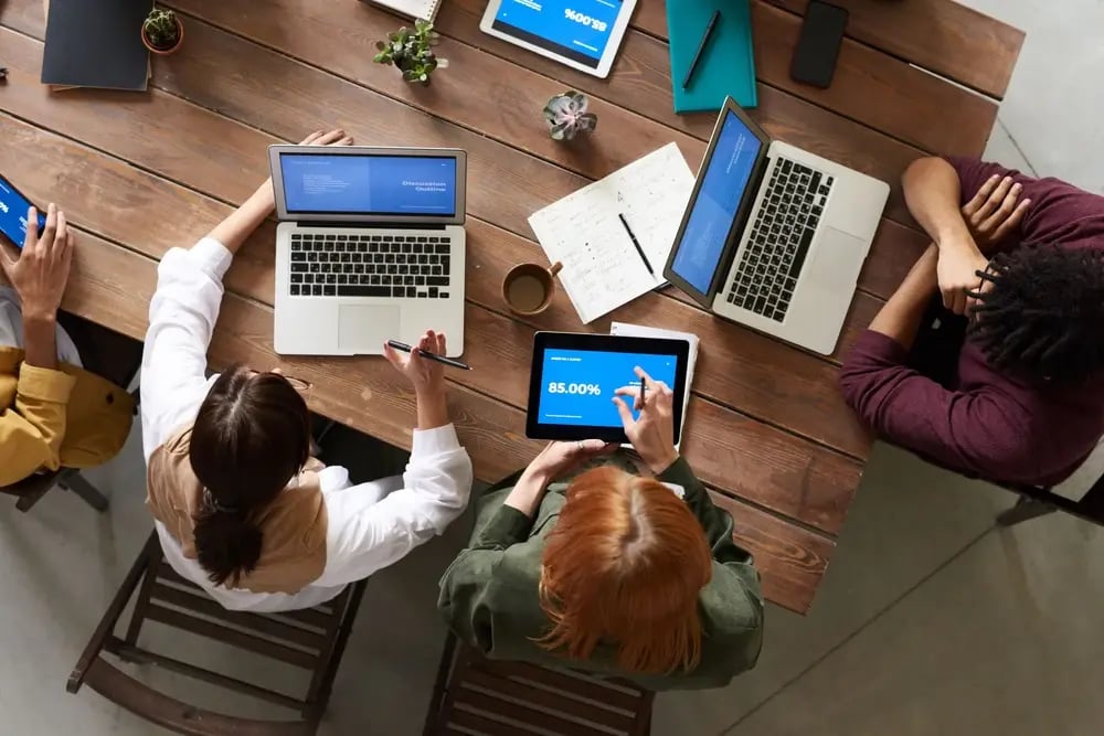 Team working on laptops and tablets around a table, seen from above